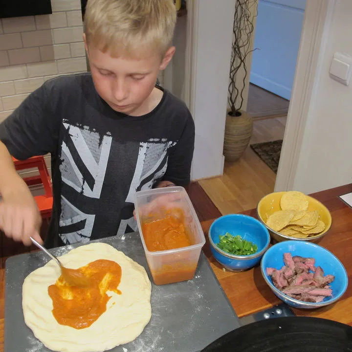 Mads legger tomatsaus på pizzaen sin.