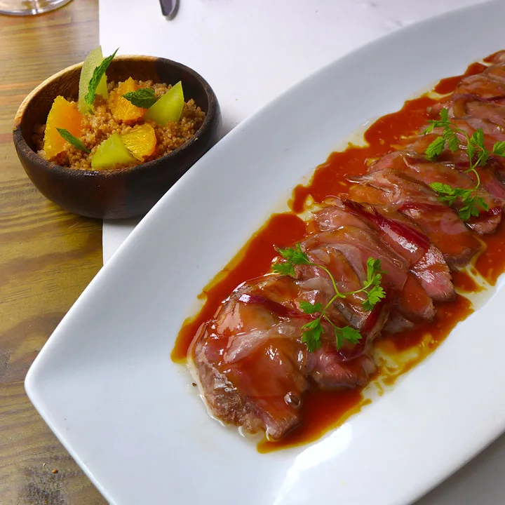 Løvtynne ibericosvin-skiver med smeltet spekeskinke på toppen servert med couscous med appelsin, eple, kanel, kardemomme